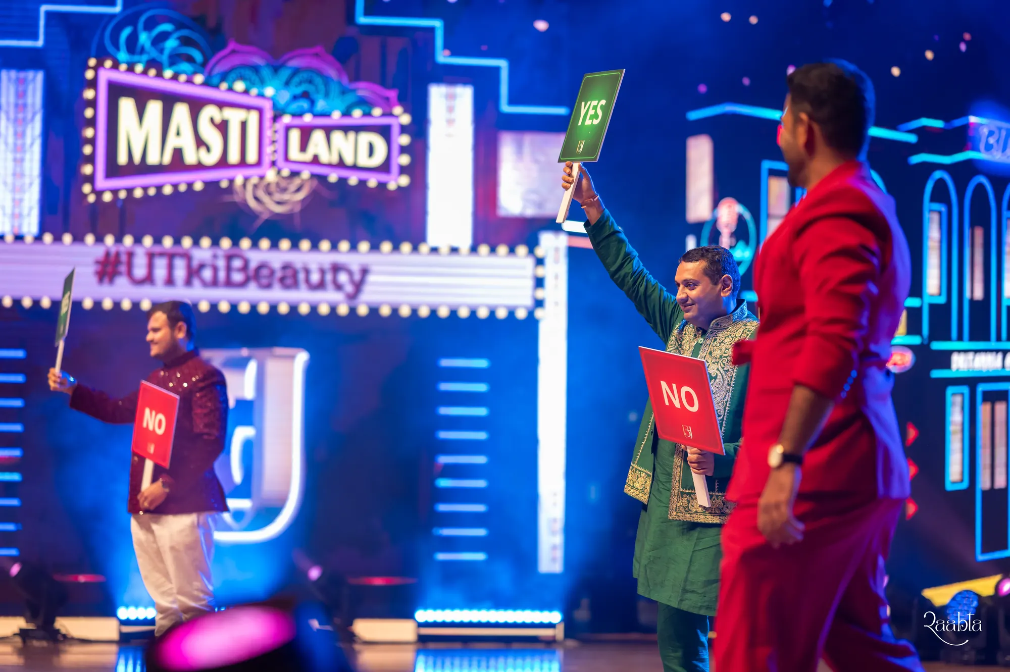 Chirag Vithalani in red on a bright game-show stage at Utkarsh and Jemimi's wedding, Abu Dhabi