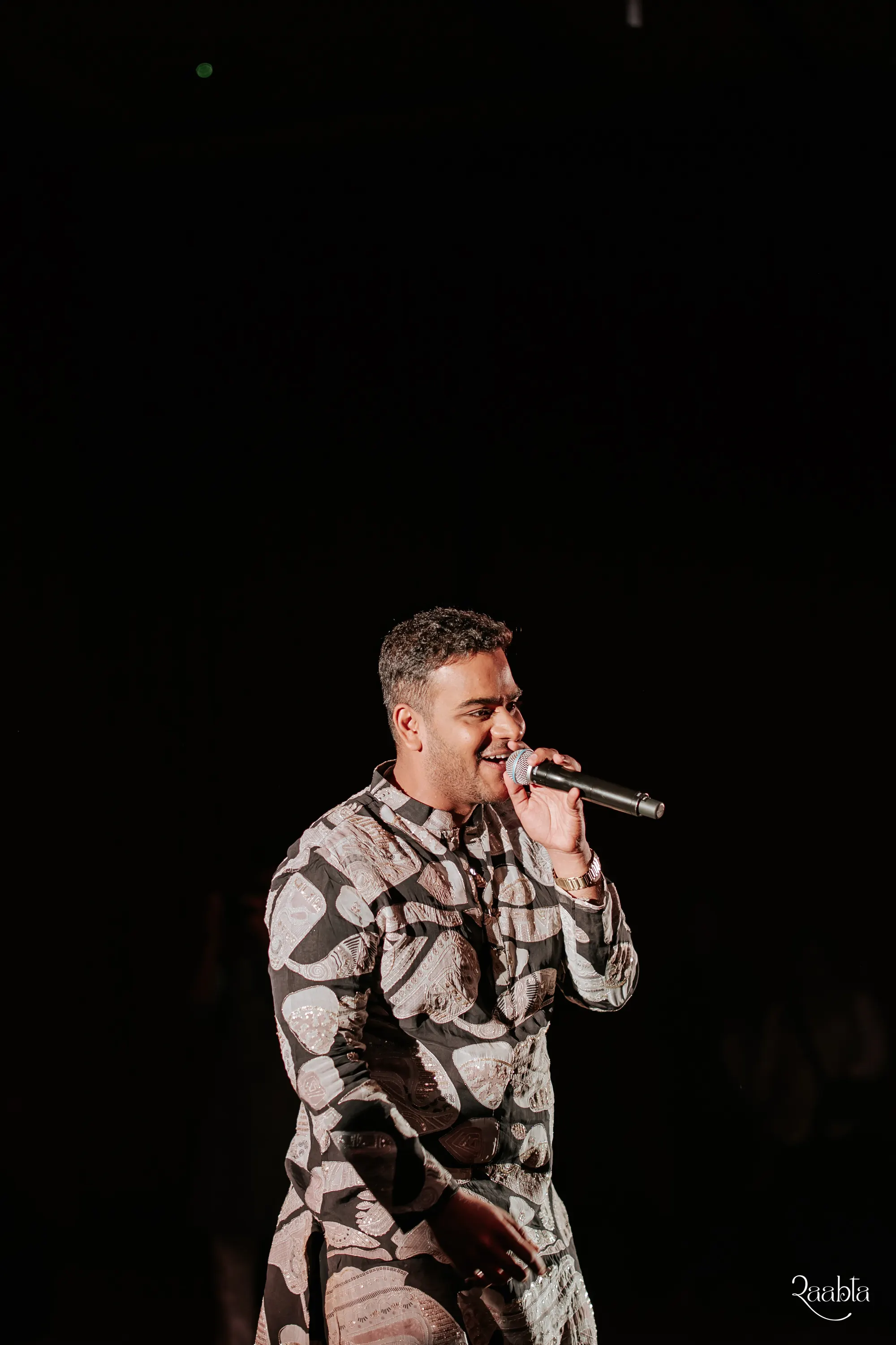 Chirag Vithalani with a microphone in a spotlight at Shiven and Palak's wedding, Bahrain