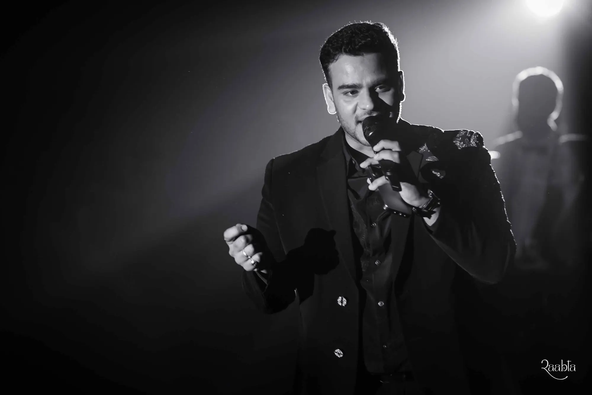 Black and white photograph of Chirag Vithalani singing into a microphone on stage