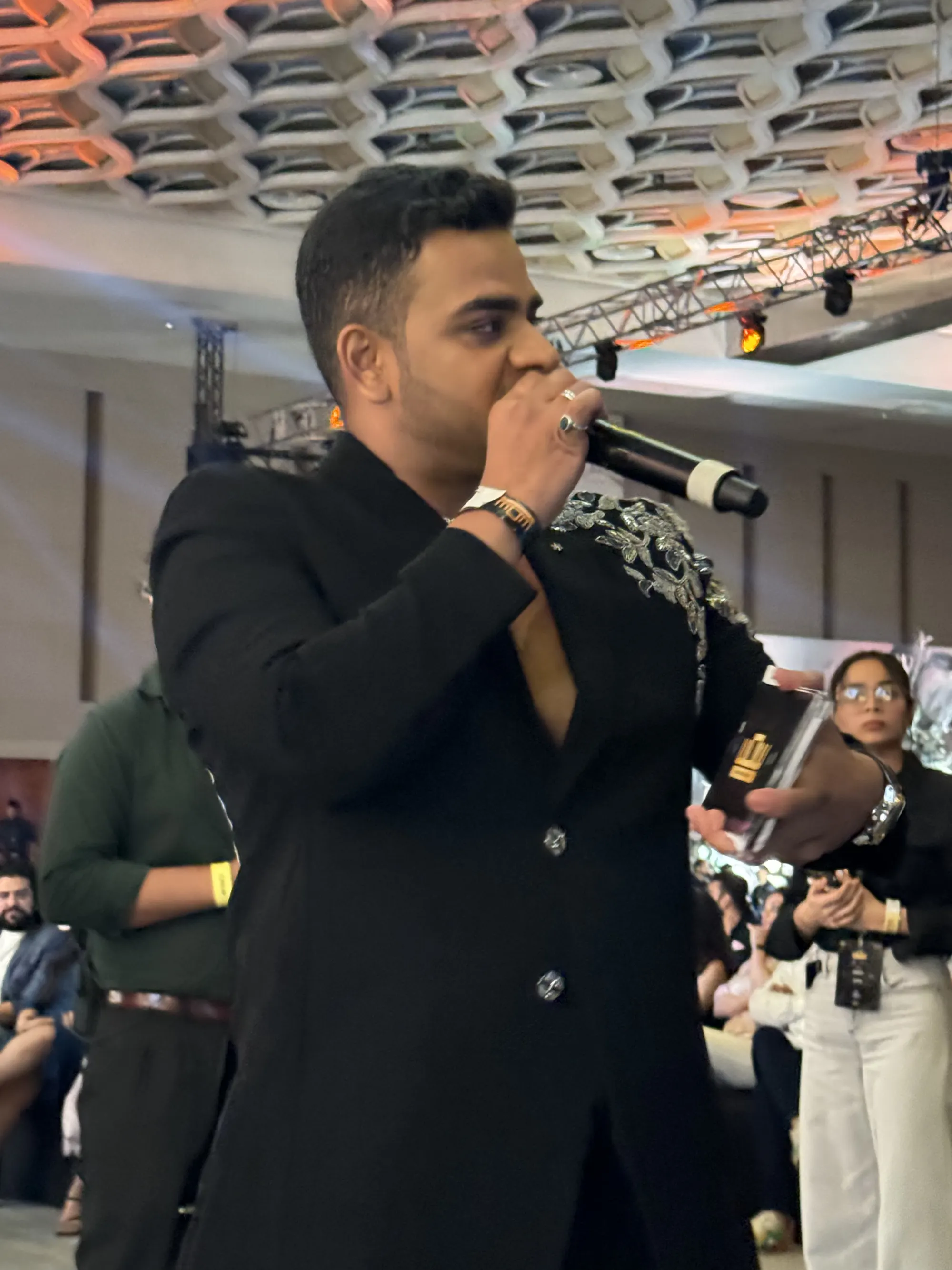 Chirag Vithalani in a black suit speaking into a microphone in the middle of the crowd