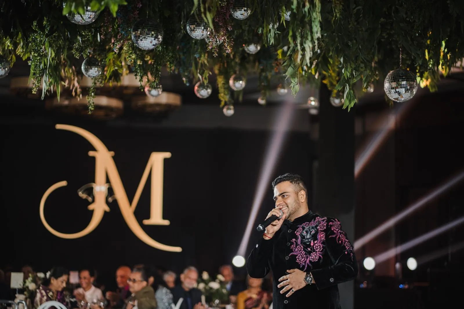 Chirag Vithalani in a spotlight beside the couple's monogram at Jenny and Mihir's reception, Phuket