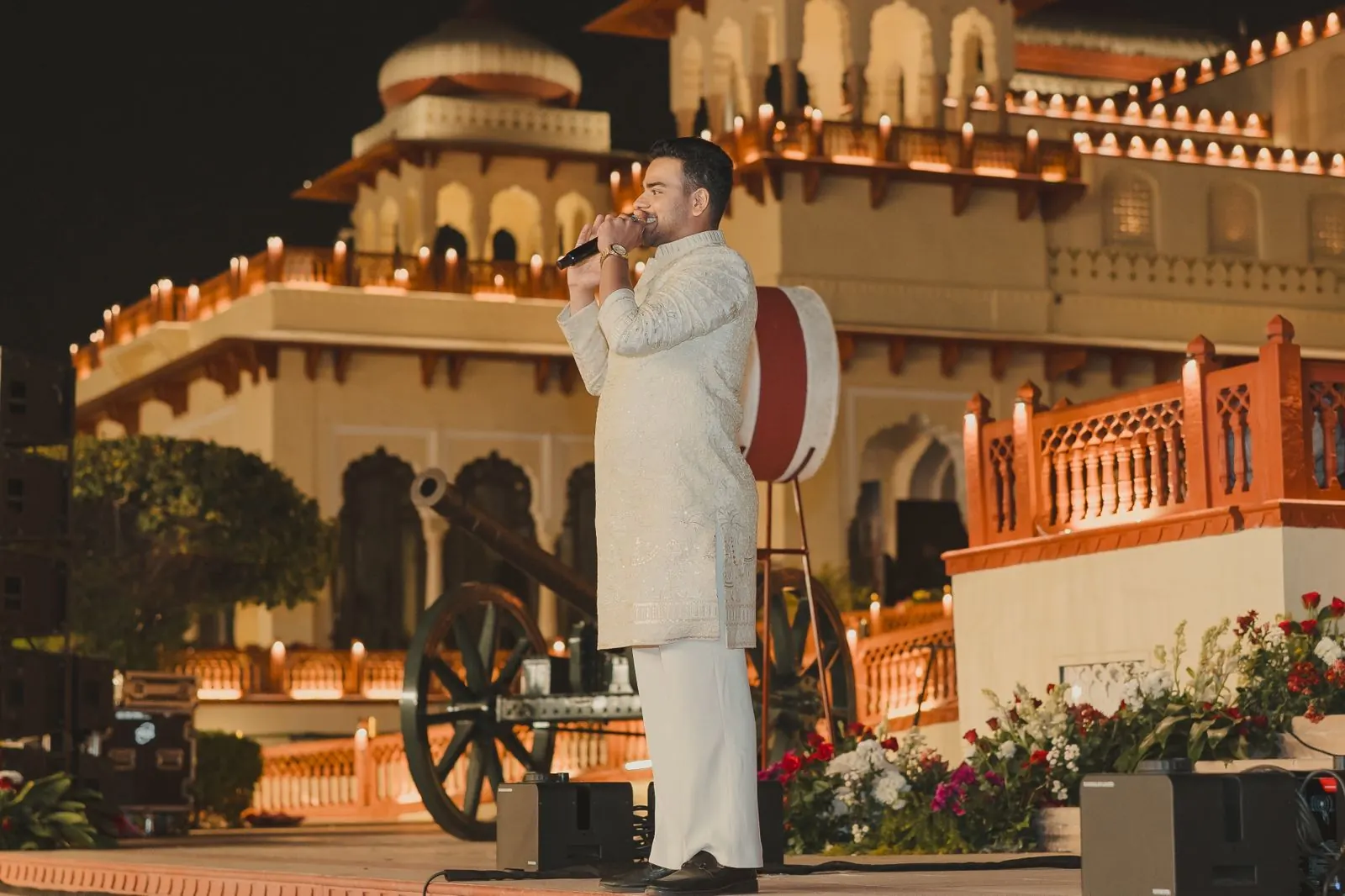 Chirag Vithalani with a microphone in front of Rambagh Palace lit up at night, Jaipur